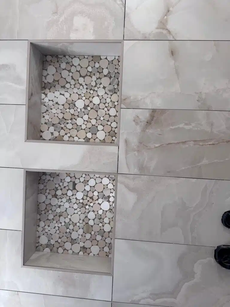 Custom tile design featuring two recessed areas filled with circular stone mosaics, surrounded by large marble tiles, emphasizing unique material selection for home remodeling.