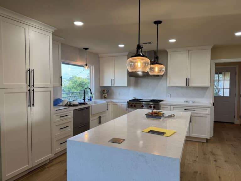 Warmly lit modern kitchen with white cabinetry and a central waterfall marble island.