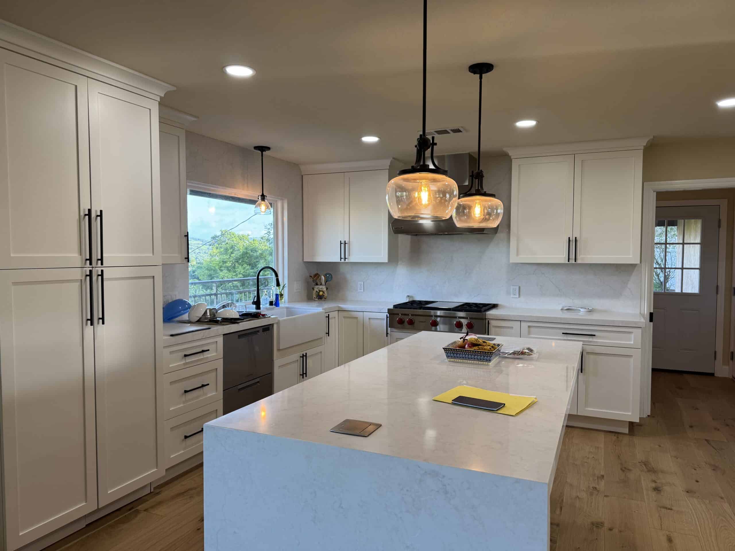 Warmly lit modern kitchen with white cabinetry and a central waterfall marble island.
