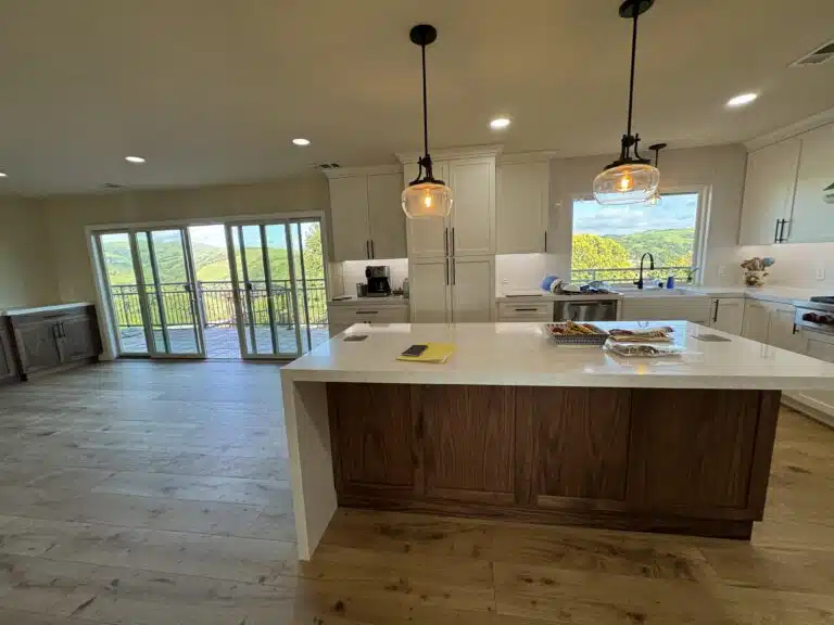 Modern kitchen with white cabinetry, wooden island, pendant lighting, and large windows showcasing a scenic view, emphasizing custom remodeling and open concept design.