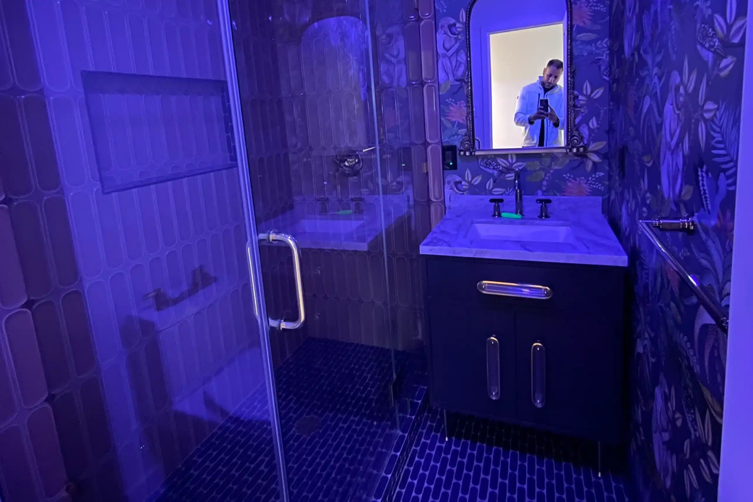 Stylish small bathroom remodel with patterned wallpaper, glass shower enclosure, and modern vanity in Los