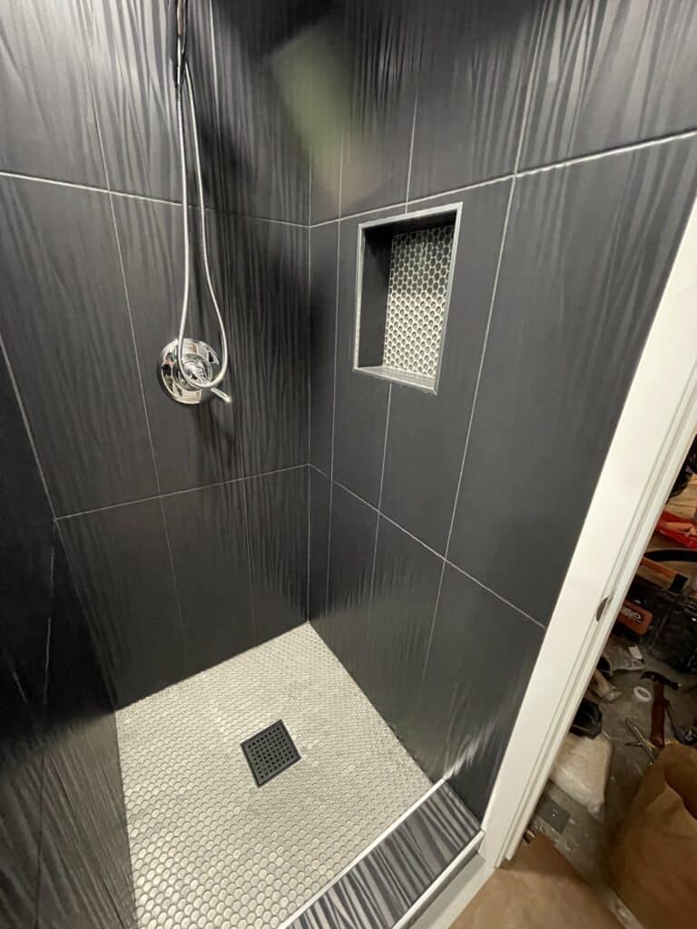 Curbless shower with dark tile, linear drain, and recessed niche showcasing waterproofing membrane.