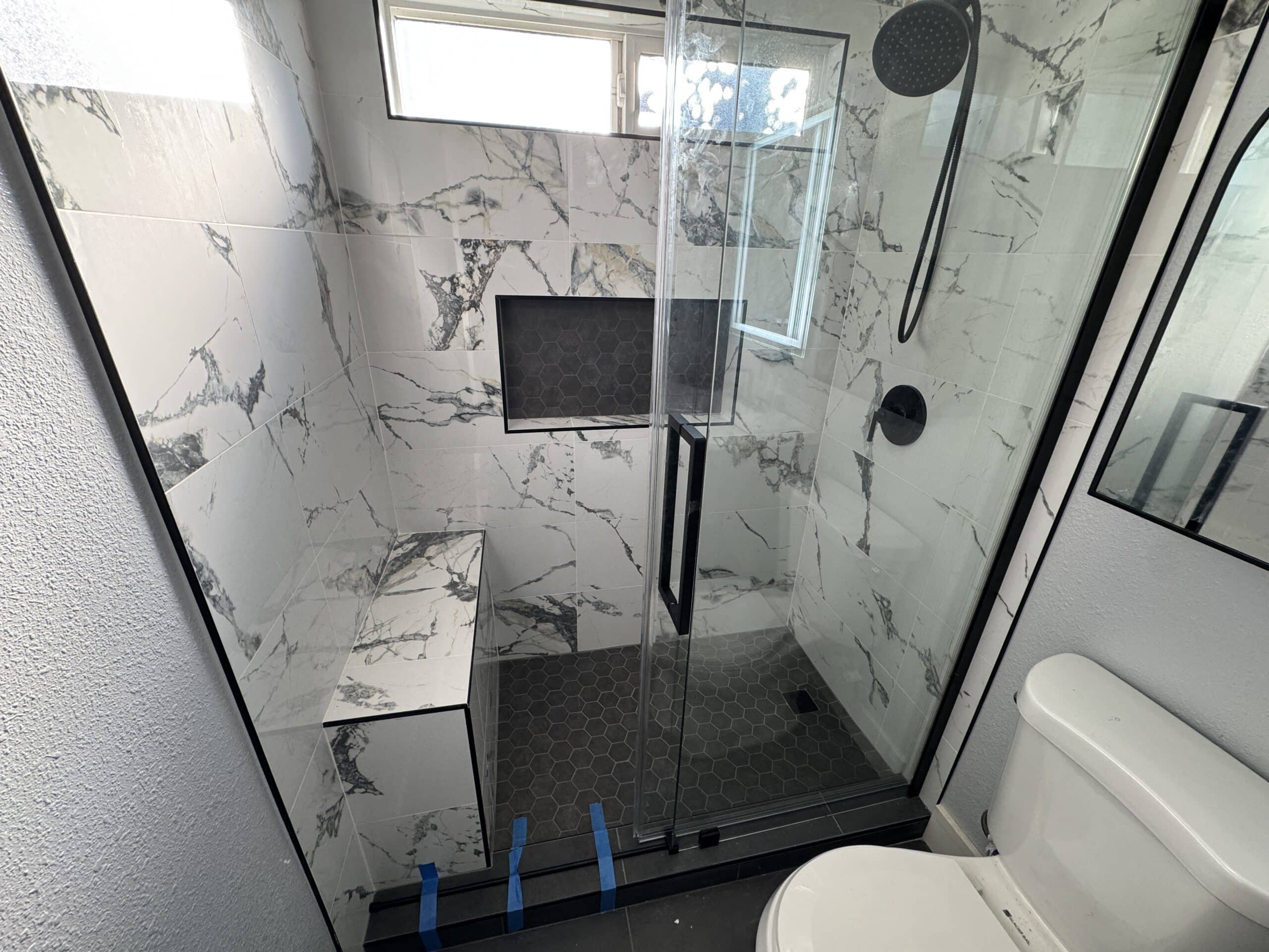 Newly renovated bathroom featuring marble-look porcelain tile and matte black fixtures, showcasing Denali Builders &