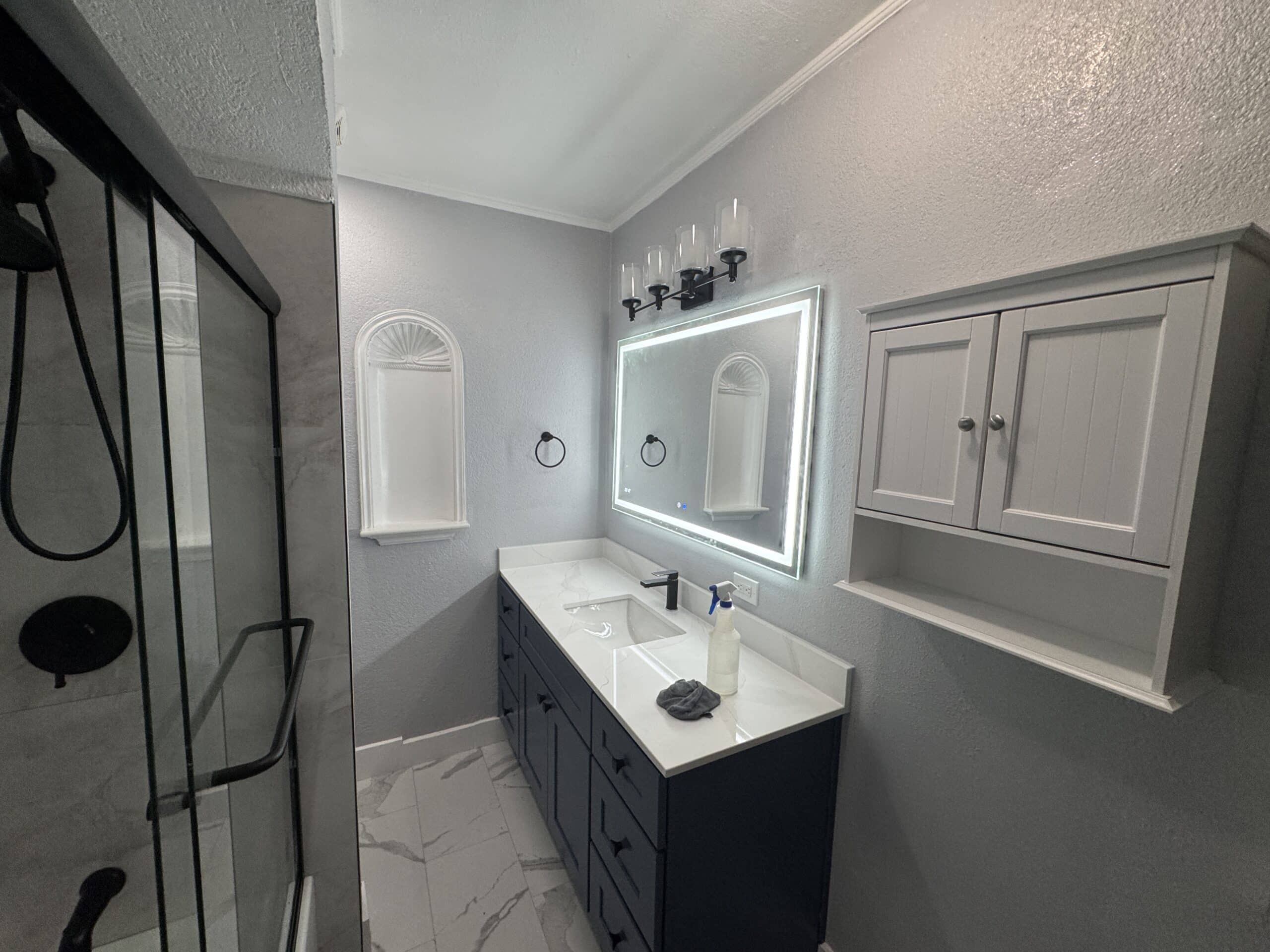 Modern bathroom with a white vanity, illuminated mirror, and glass shower