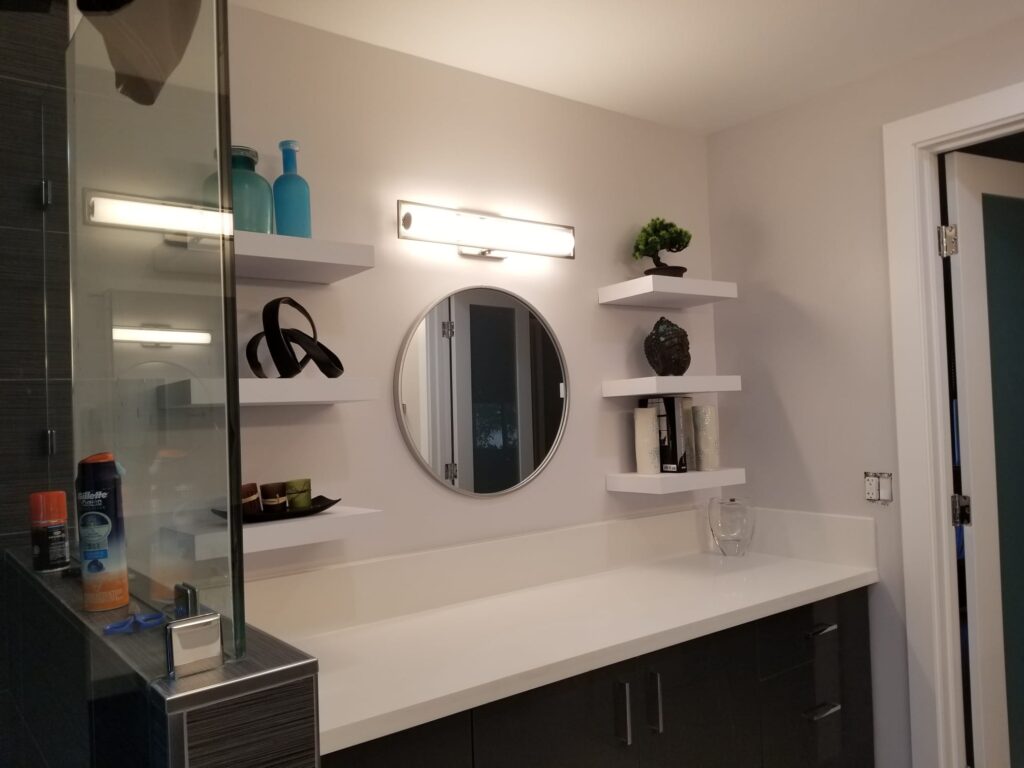Modern master bathroom remodel in Los Angeles with floating shelves, round mirror, and custom walk-in
