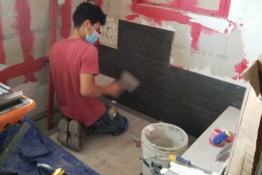 Contractor installing tile in bathroom renovation, waterproofing membrane visible, curbless shower construction in Los Angeles.