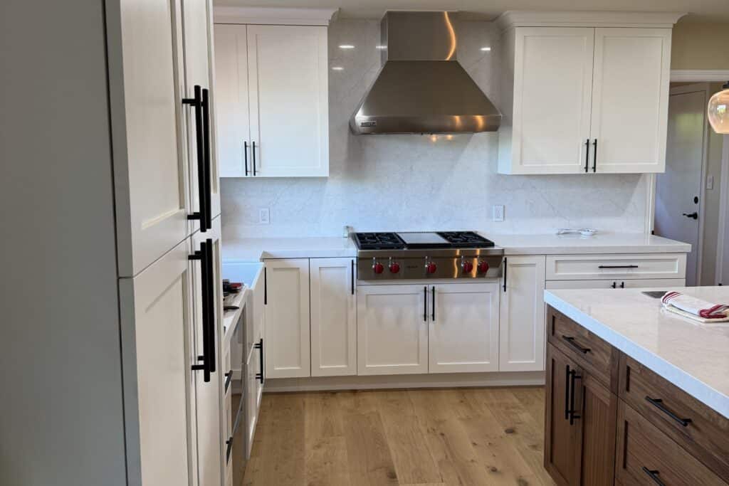 Straight-on view of a stainless steel gas range, range hood, white cabinets, and wood kitchen island.