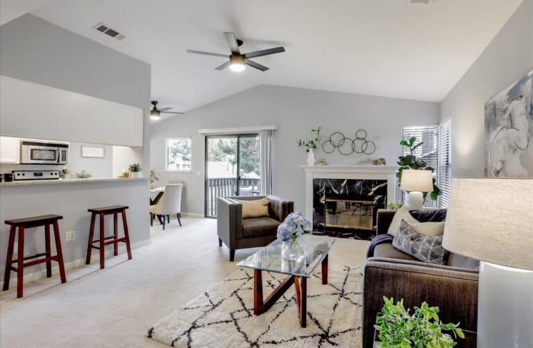 Finished living room with vaulted ceiling, marble fireplace, gray sofa, and breakfast bar stools.