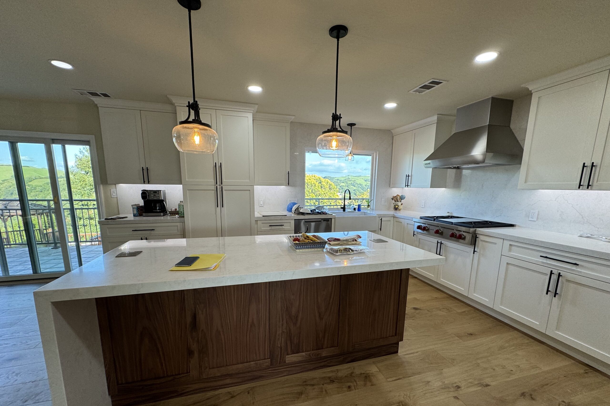 Close-up of a kitchen island with pendant lighting, stainless steel range hood, and scenic view outside.