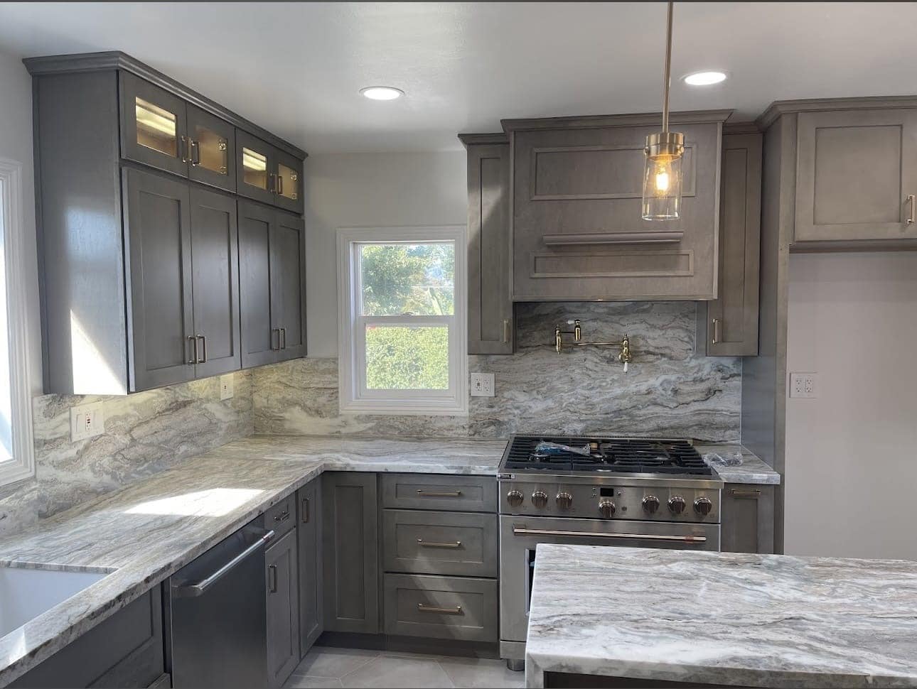 Riverside kitchen remodel featuring warm gray shaker cabinetry, a stone backsplash, and stainless steel appliances
