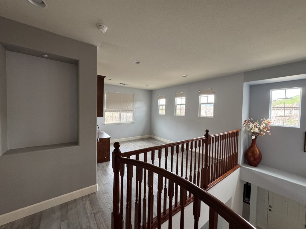 Open upper-level floor plan with wood-look flooring and dark wood railing, showing existing second-story layout before renovation.