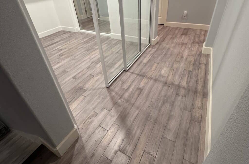 Hallway in a remodeled Pasadena home with new gray-brown wood-look plank flooring, white baseboards, and mirrored sliding closet doors.