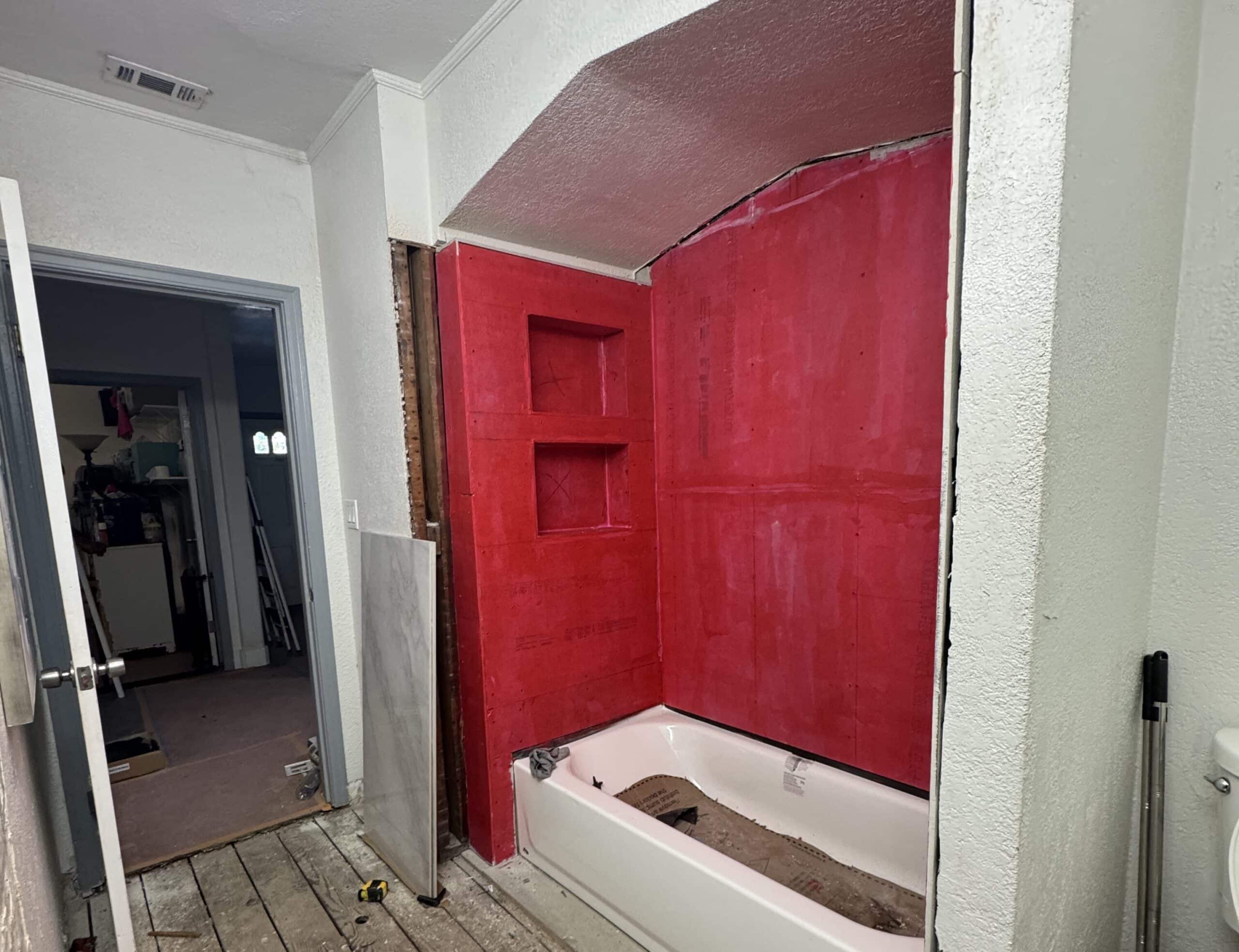 Active bathroom remodeling project of a bathroom with a red wall around the bathtub