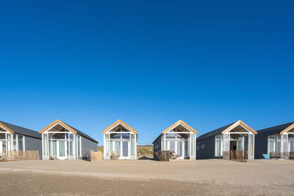 Row of modern beach cabins with large windows, set against a clear blue sky, representing